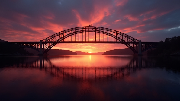 Silhouette of an arched bridge against a vibrant sunset sky with dramatic layered clouds over calm water