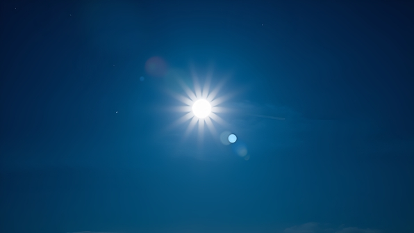 Bright full moon shining vividly against a clear deep blue evening sky with wisps of clouds and twinkling stars