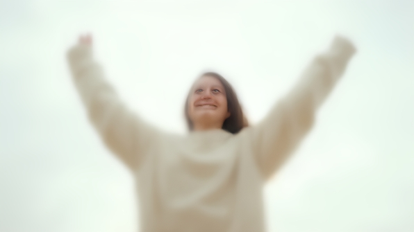 A person in a cozy white sweater joyfully raising their hands against a bright overcast white sky