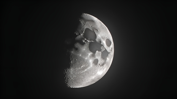 Detailed half moon close-up showing lunar craters and textured surface against a dark night sky in grayscale