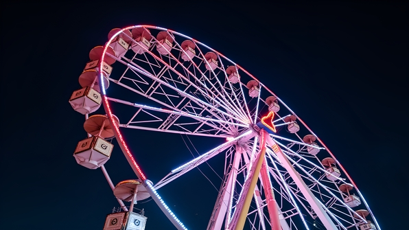A vibrant close-up of a ferris wheel illuminated with colorful lights against a dark night sky