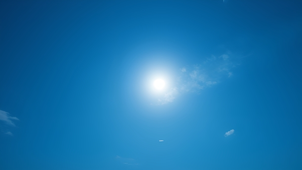 A bright white full moon glowing softly against a clear, vibrant blue daytime sky with subtle wisps of clouds