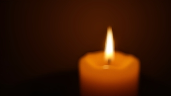 Close-up of a glowing yellow candle with a flickering flame creating a warm, cozy ambiance