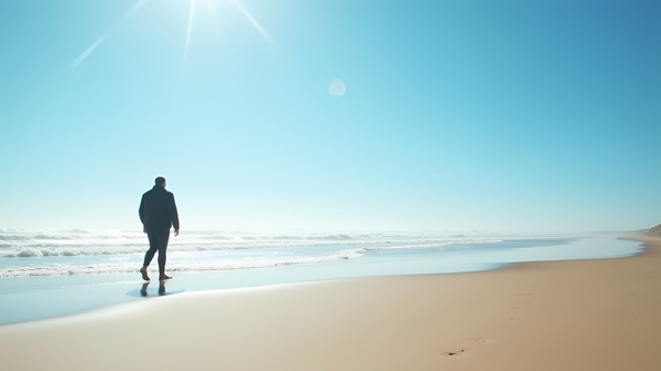 Man in black jacket walking along a sandy beach under bright daylight and clear blue sky
