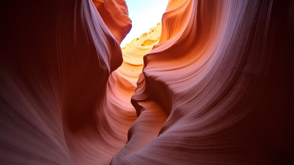 A narrow winding slot canyon featuring smooth red sandstone walls illuminated by warm sunlight filtering from above