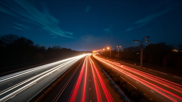 Nighttime time-lapse of bright highway lights showing cars streaking along a busy road under a starry sky