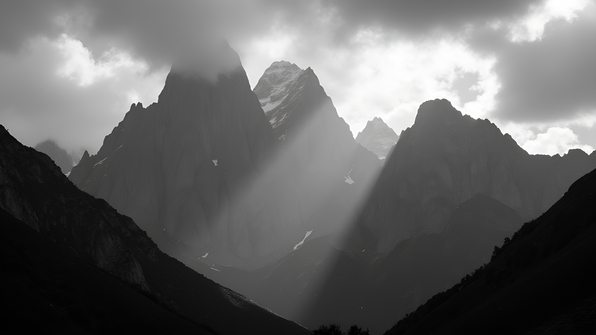 High-contrast black and white photograph of a rugged mountain range with sharp peaks and dramatic shadows under a cloudy sky