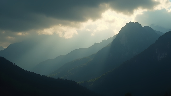 Silhouette of a rugged mountain range beneath a cloudy sky with soft sunlight filtering through