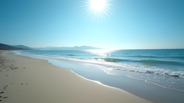 Serene rippling ocean gently meeting a sandy coastline under a clear blue sky with distant hills on the horizon