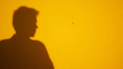 Silhouetted Figure Casting Sharp Shadow On Yellow Wall