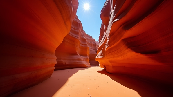 Sunlit narrow sandstone canyon featuring smooth, flowing orange and red rock formations under a clear blue sky