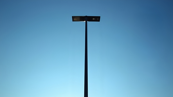 A tall slender black metal post standing alone against a clear blue sky on a sunny day