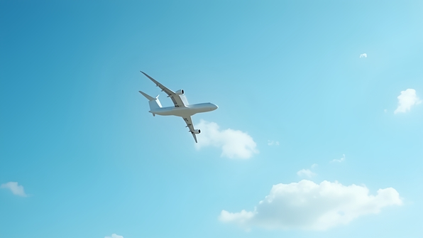 White commercial airplane flying in blue sky with soft clouds and sunlight reflecting off wings