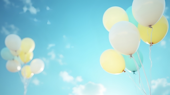 Clusters of white and yellow balloons floating gently against a clear blue sky with scattered soft clouds
