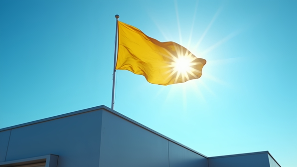 Yellow and blue flag waving atop a modern rooftop against clear blue sky on a sunny day