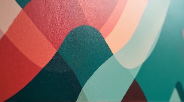 Close-up of abstract emerald and crimson shapes diagonally arranged on a canvas under soft lighting
