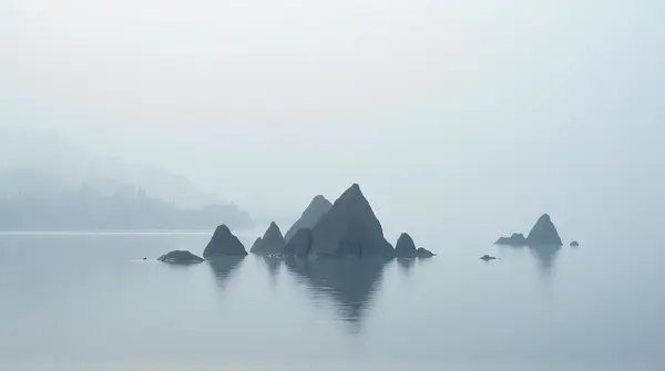 Cluster of angular stone formations reflected in a lake under a soft grayish-white sky