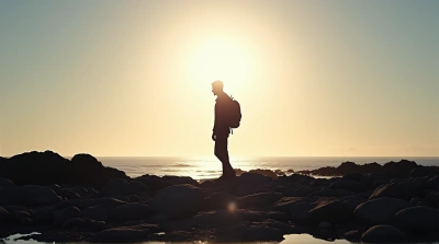 Backlit Figure On Rocky Shore With Glowing Sky