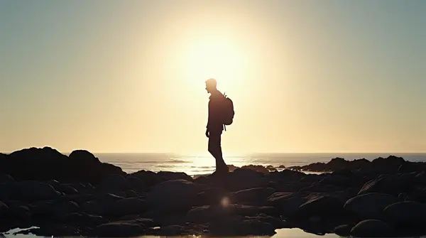 Backlit Figure On Rocky Shore With Glowing Sky