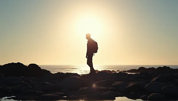 Backlit Figure On Rocky Shore With Glowing Sky