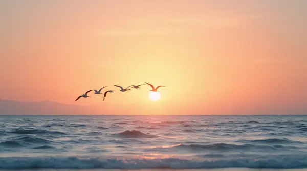 A group of birds flying above a calm ocean under an orange and pink evening sky with soft reflections on the water.