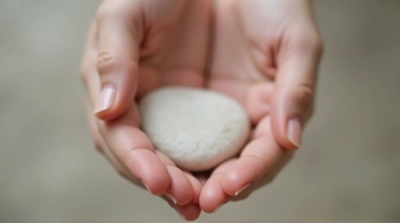 Close-Up Of Fingers Grasping Pale Oval Pebble