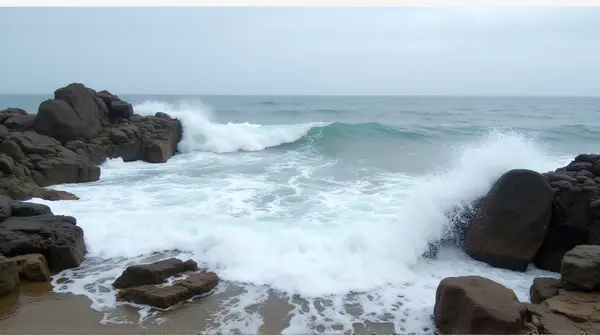 Waves breaking onto jagged rocky shore with foamy spray under a cloudy sky from low angle