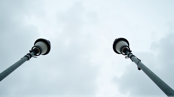 Two metal lampposts with intricate designs converging upward against a cloudy sky