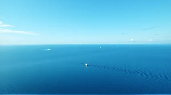 Overhead shot of vast blue sea with whitecaps and a distant sailboat under clear sky