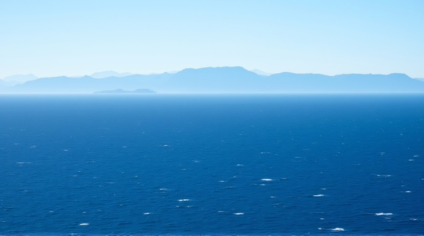 Vast deep blue sea extending to horizon with small waves and distant mountains in background