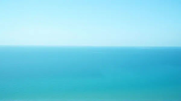 Vast deep sea extending to the horizon beneath a clear sky from a low shore perspective