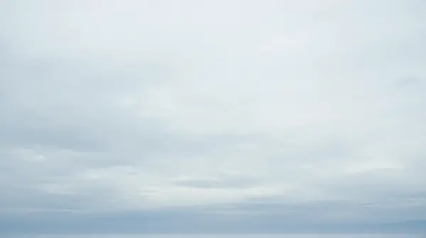 Wide view of layered pale silver and muted white clouds stretching across the horizon from a low angle