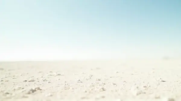 Vast pale granular land under a clear bright sky with soft sunlight and gentle shadows