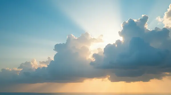 Wide sky packed with large nimbus clouds lit by warm sunlight above a distant horizon.