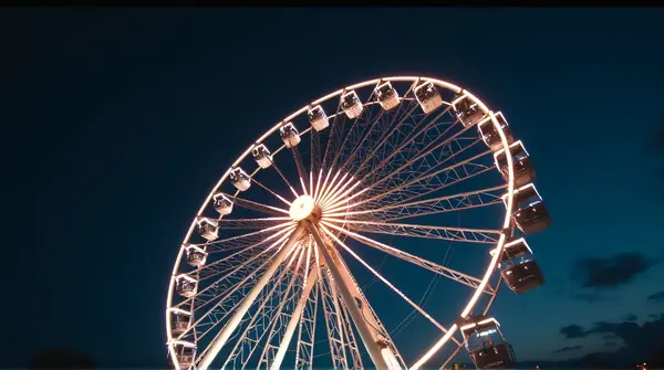 Low angle view of a glowing ferris wheel with spokes radiating against a dark sky in soft focus