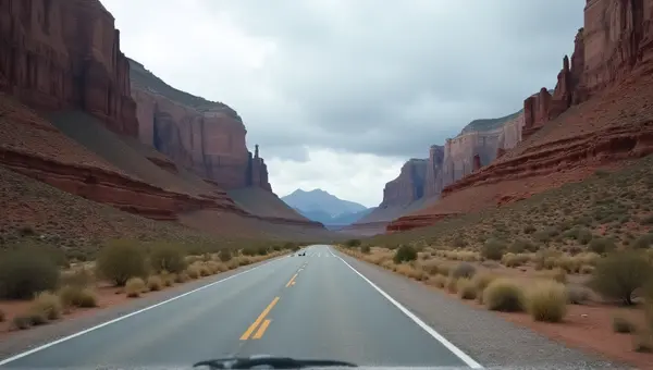 Gray Asphalt Path Beside Towering Cliffs Under Clouds