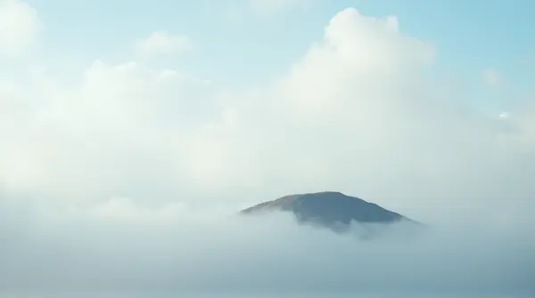 An isolated island beneath fluffy white clouds with soft shadows and a low horizon during daylight.
