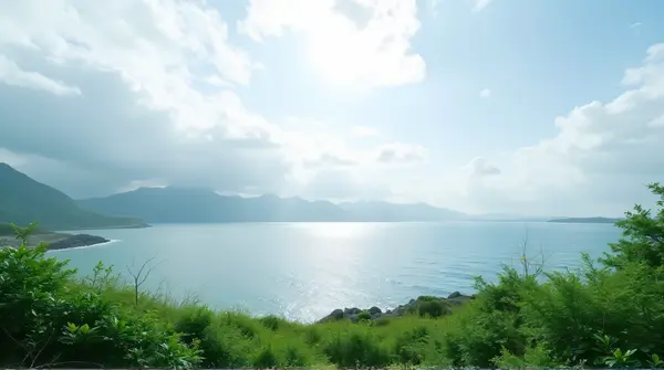 Dense green foliage beside a calm body of water under a broad cloudy sky in a wide horizontal view.
