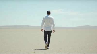 Man Striding Across Open Terrain Under Clear Sky