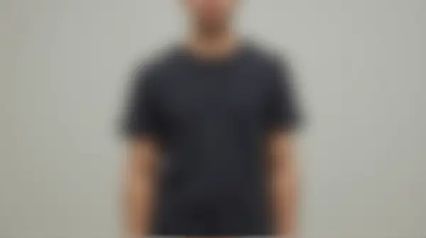 A man stands with arms relaxed by his sides wearing a dark crew-neck t-shirt against a soft neutral backdrop.