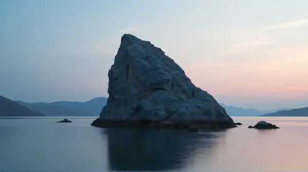 Large stone formation rises from still water under fading dusk sky with dark distant terrain silhouettes