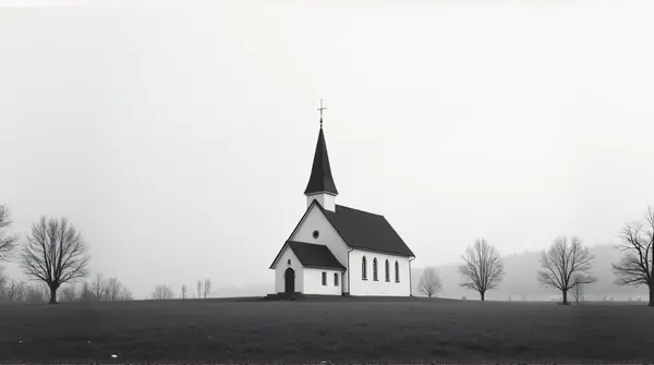 Black and white church with leafless trees in a grassy clearing under a wide sky
