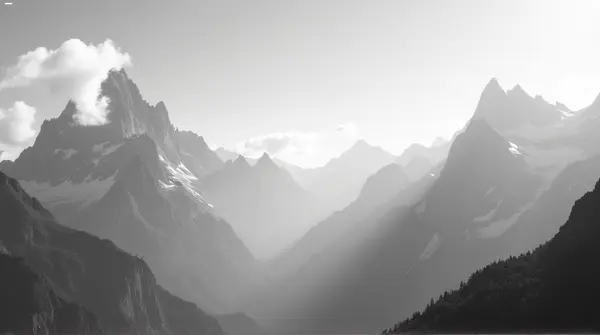 Monochrome towering mountain peaks with sharp ridges under a bright sky and wispy clouds casting defined shadows.