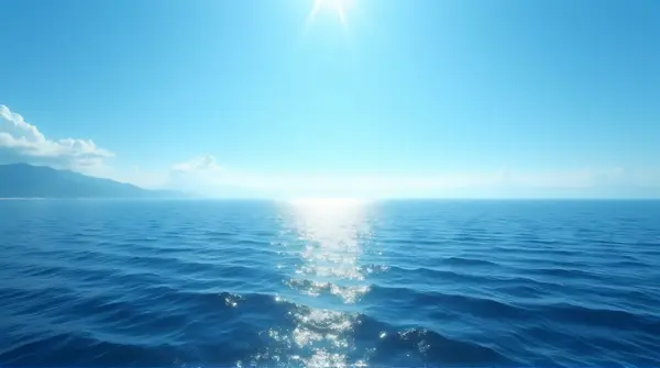 Sunlight reflects on rippling ocean surface beneath a clear sky and misty distant coast.