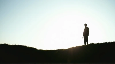 Person Standing On Grassy Rise Against Bright Sky