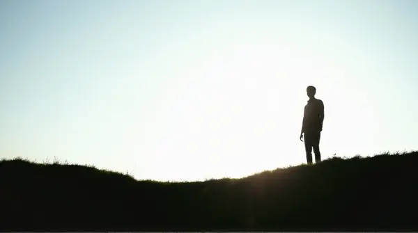 Figure outlined against bright sky on grassy rise from low angle emphasizing contrast