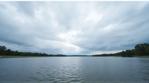 Wide rippling lake under layered gray and white clouds with trees in the distance.