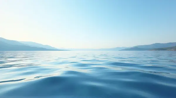 Wide rippling water reflecting a clear blue sky and rolling hills under soft daylight