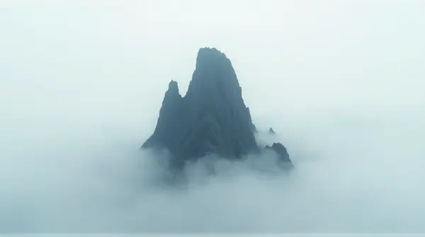 A tall rocky peak piercing misty vapor under a pale sky seen from below emphasizing height and solitude.