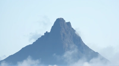 Rocky Summit Shrouded In Mist Under Pale Blue Sky